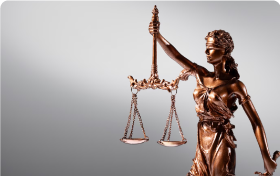 Imagem do símbolo da justiça em bronze com fundo cinza.